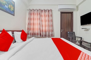 Quarto de hotel com cama, televisão, escrivaninha e uma cadeira.