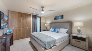 Une chambre d’hôtel équipée d’un lit, de tables de chevet, d’un bureau, d’un ventilateur de plafond et d’œuvres d’art accrochées aux murs.