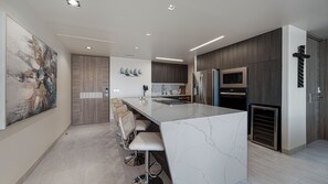 A modern kitchen with a marble island, stainless steel appliances, and a seating area with bar stools. - Two 1507: Luxury Above the Sea Of Cortez (Puerto Peñasco)