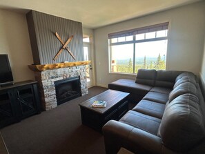 Ein Wohnzimmer mit Kamin aus Stein, einer Ledersofa, einem Couchtisch und einem Fernseher.