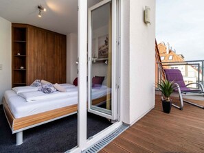 A bedroom with a bed, wardrobe, and a sliding glass door leading to a balcony with a chair and a potted plant. - Holiday Apartment With 3 Bedrooms (Grossenbrode)