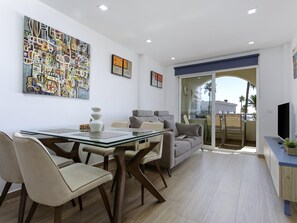 A modern living room with a glass dining table, comfortable seating, and artwork on the walls. - Sunstay Flat Los Alamos Beach (Torremolinos)