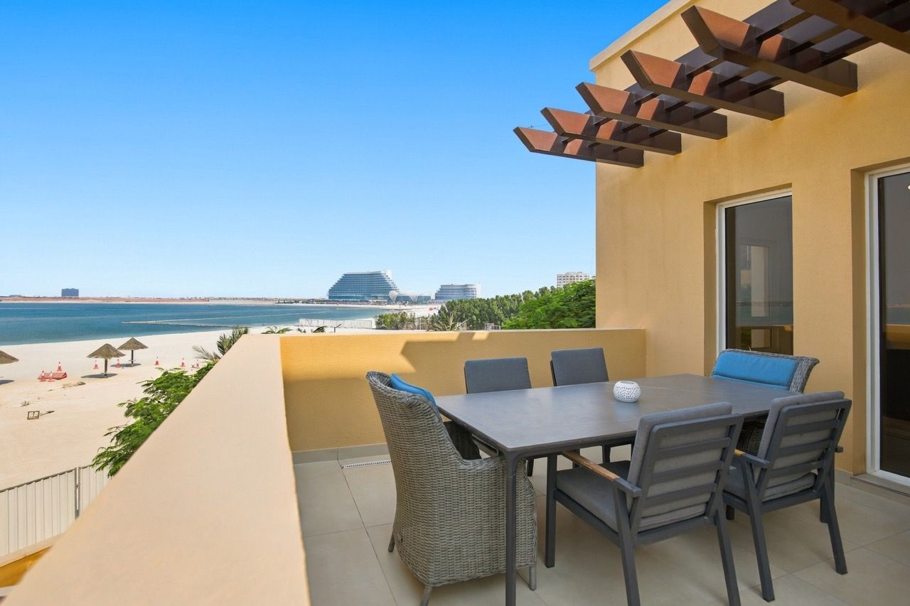Een balkon met een tafel en stoelen, met uitzicht op een strand en de oceaan.