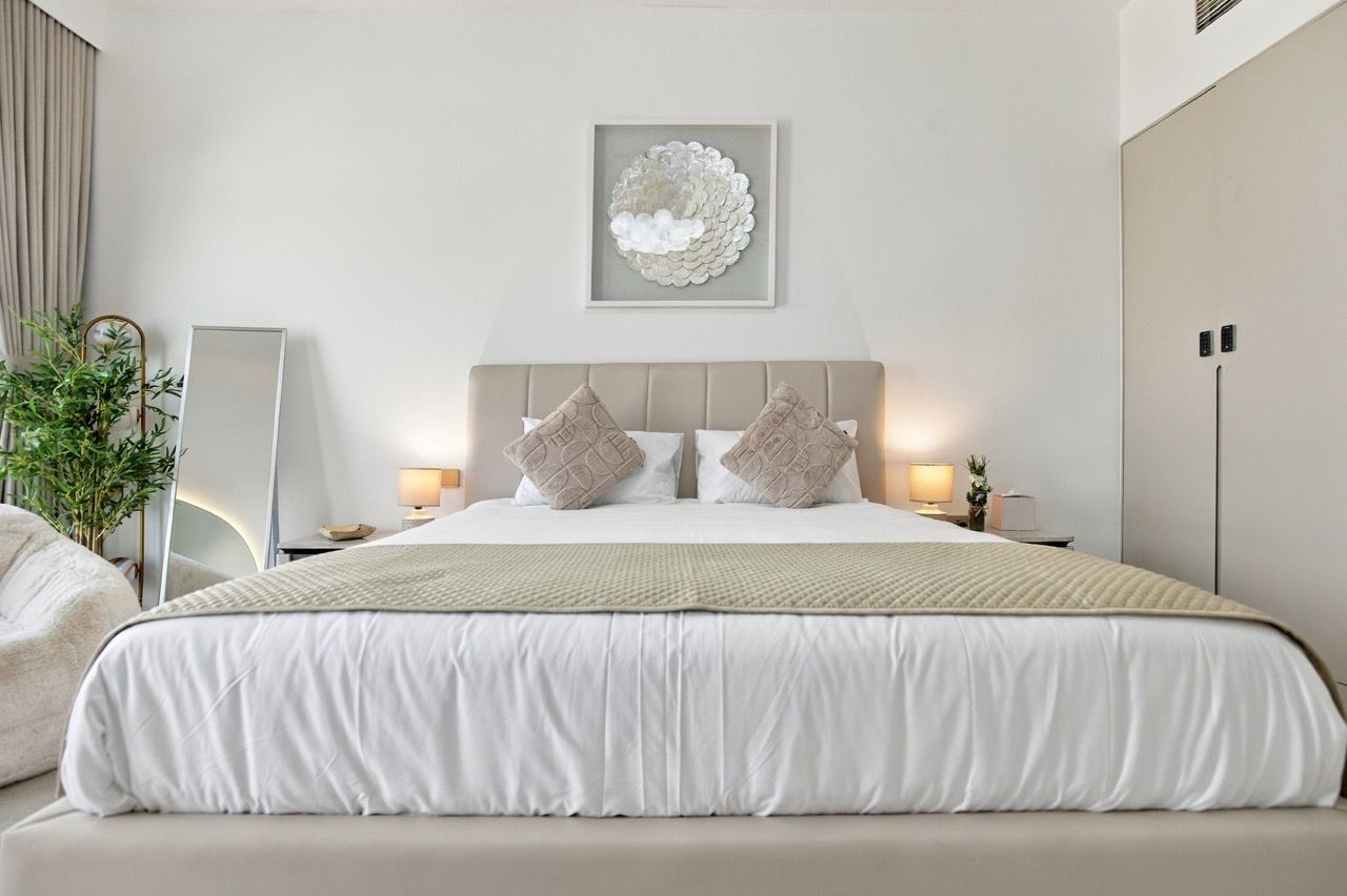 Een moderne slaapkamer met een groot bed, twee nachtkastjes met lampen, een kunstwerk aan de muur en een plant.