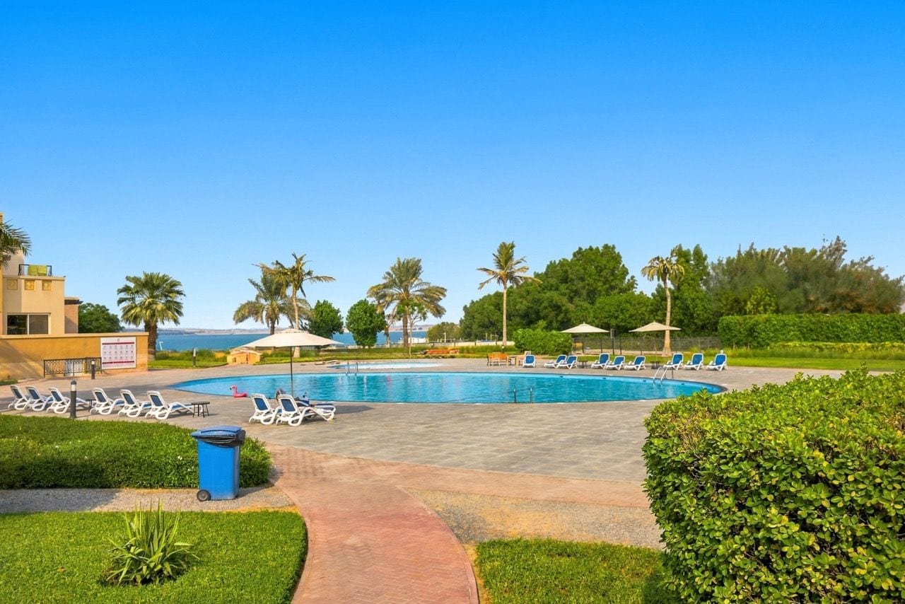 Ein Poolbereich mit Liegestühlen, Palmen und blauem Himmel.