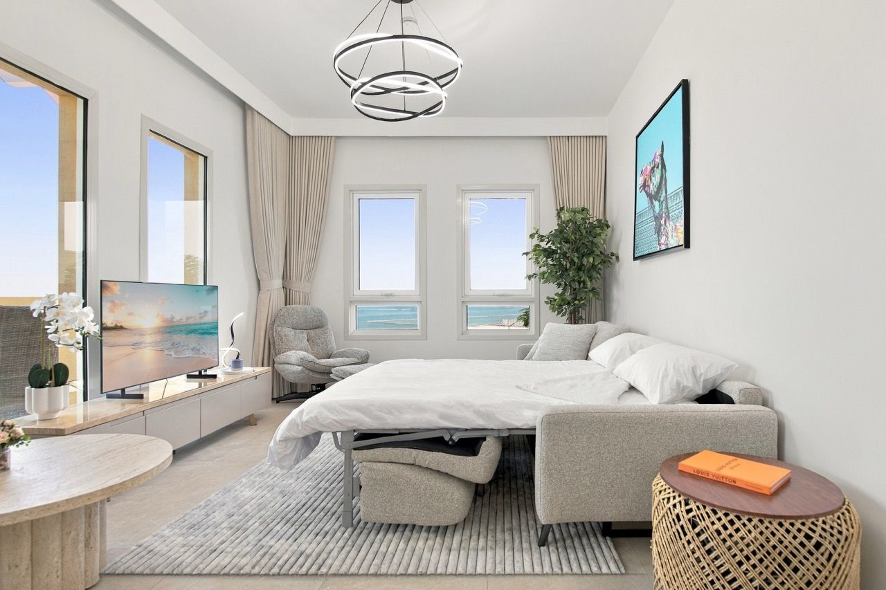 A modern bedroom with a bed, a TV, a chair, a small table, and a plant.