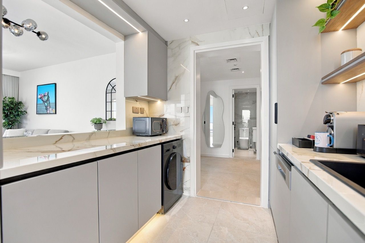 A modern kitchen with a built-in washing machine, a microwave, and a coffee machine.
