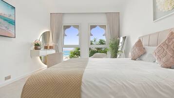 A bedroom with a large bed, a view of the sea through a window, and a bedside table with a lamp.