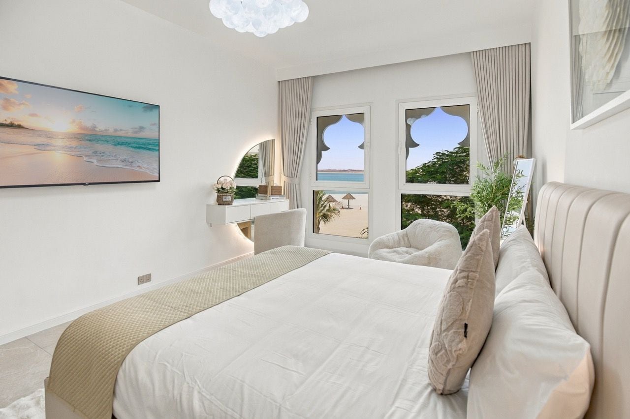 Una camera da letto con un letto grande, una TV, una scrivania e vista sul mare dalle finestre.