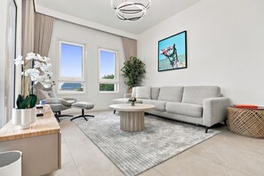 A modern living room with a grey sofa, a round coffee table, a chair, a potted plant, and a large window with a view. - Cozy Newly Full Renovated 1-bedroom Apartment With Full Seaviews From Every Room (Ras Al Khaimah)