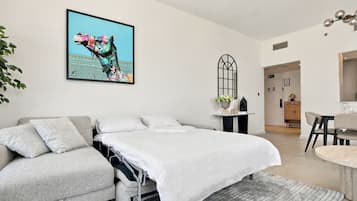 Ett modernt sovrum med en säng, en grå soffa, en matplats och ett konstverk som hänger på väggen.