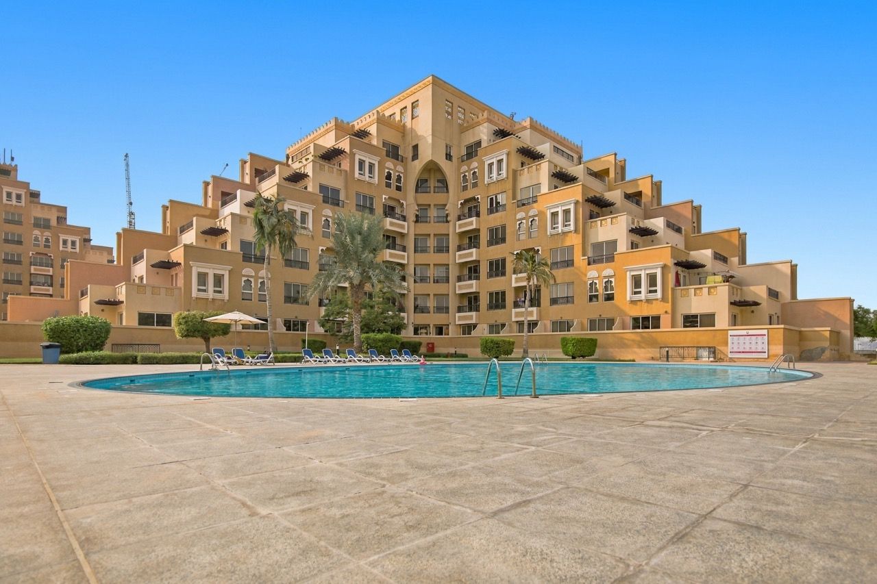 A multi-story hotel with a swimming pool surrounded by lounge chairs.