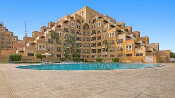 A multi-story hotel with a swimming pool surrounded by lounge chairs.
