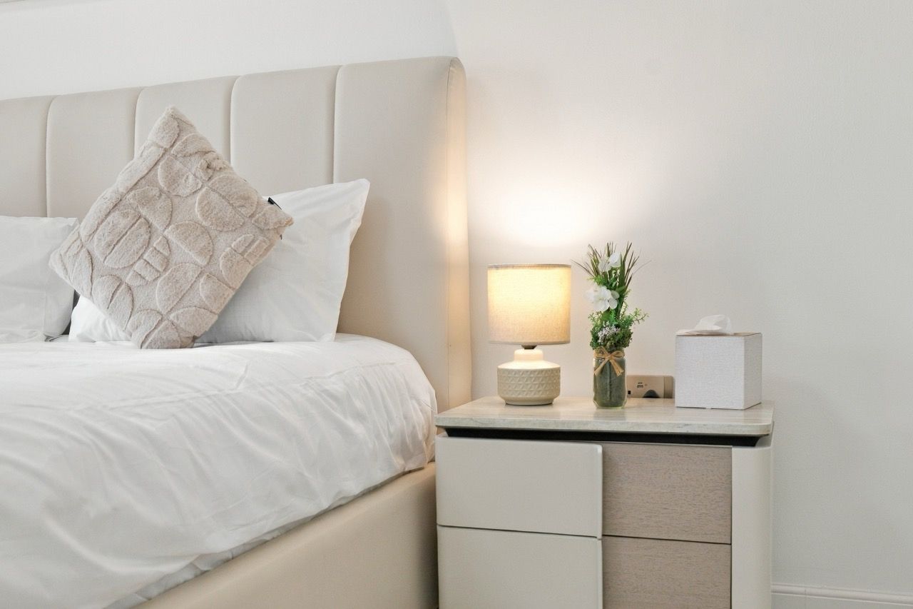 A neatly made bed with a pillow, a bedside lamp, and a small vase with flowers on a bedside table.