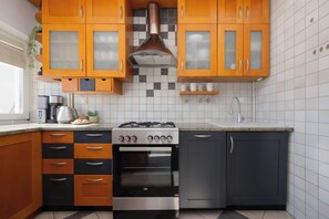 A traditional-style kitchenette with wooden cabinets, a gas stove, a sink, and a refrigerator. White tiled walls and dark countertops create a practical cooking space. - Warsaw | Solidarności Avenue 92 | Two-storey Apartment | Balcony (Warszawa)