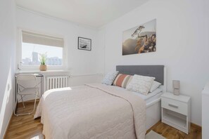 Ein Schlafzimmer mit Bett, Nachttisch, Fenster und Blick auf die Stadt.