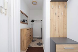 A hallway area with a wooden wardrobe providing plenty of storage space. A small chest of drawers and a mirror are also visible, with a doorway leading toward another room. - Warsaw | Solidarności Avenue 92 | Two-storey Apartment | Balcony (Warszawa)