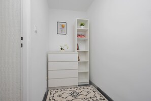 Ein heller Innenraum mit einem weißen Kleiderschrank, einem Regal mit einer Pflanze und einem gerahmten Bild an der Wand.