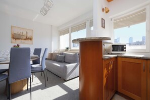 A modern kitchen with a microwave, a dining area with chairs and a table, and a sofa. - Warsaw | Solidarności Avenue 92 | Two-storey Apartment | Balcony (Warszawa)
