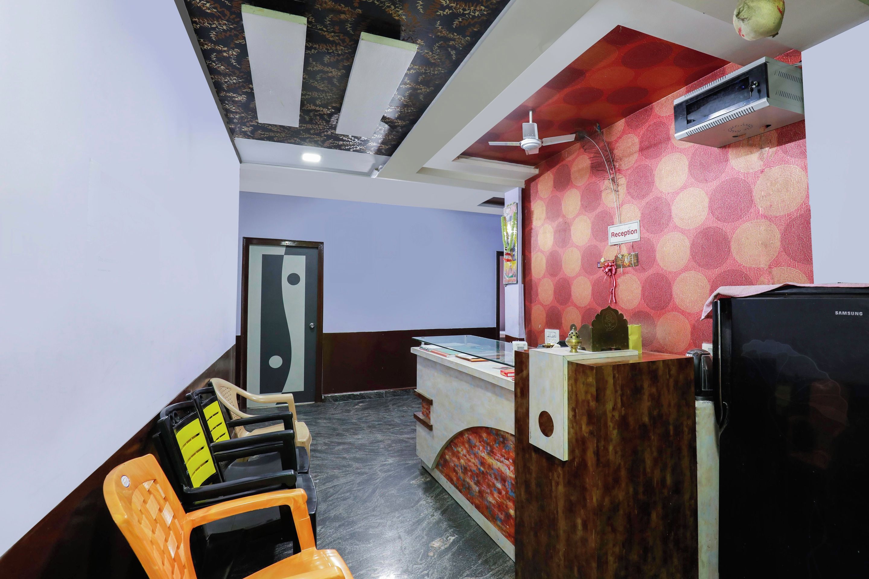 A reception area with a reception desk, a black refrigerator, and a ceiling fan.