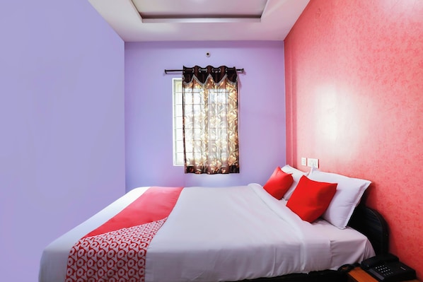 A bedroom with a bed, a window with curtains, and a wall socket. - Hotel O Qualia Grand (Hyderabad)