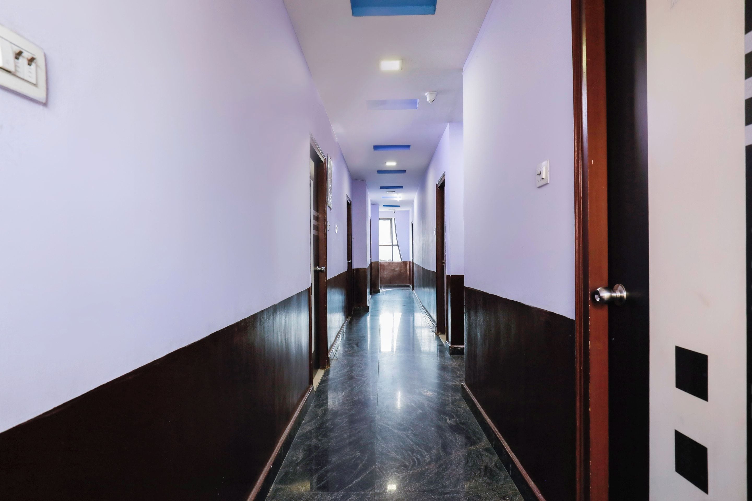 Un pasillo con puertas a ambos lados, piso de mármol e iluminación empotrada en el techo.