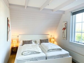 A bedroom with a sloped ceiling, two beds, bedside lamps, and a window with a view. - Se06 Holiday Home Serooskerke (Serooskerke)