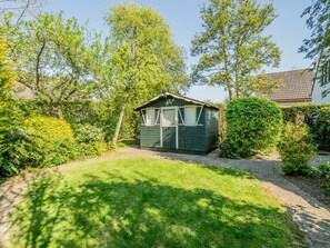 A small, single-story wooden structure with a sloped roof, surrounded by a well-maintained lawn and dense shrubbery. - Holiday Home With 3 Bedrooms (Burgh-Haamstede)