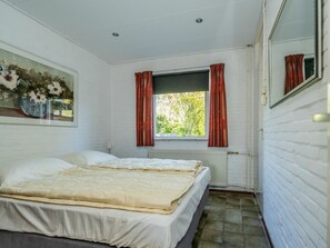 A bedroom with a bed, a window with curtains, a radiator, and a painting on the wall. - Holiday Home With 3 Bedrooms (Burgh-Haamstede)