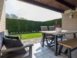 Eine Terrasse im Freien mit Tisch, Stühlen, einer Bank und einer Backsteinmauer.