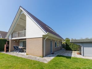 Ein eingeschossiges Haus mit geneigtem Dach, einem Balkon und einer kleinen Terrasse mit Gartenmöbeln.