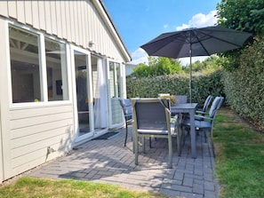 A patio with a table and chairs, an umbrella, and a house with a sliding glass door. - Ok17 Holiday Home Oostkapelle (Oostkapelle)