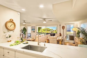 A kitchen with a marble countertop, a sink, and a dining area with wicker furniture. - Gorgeous Kaanapali 3BR with Dreamy Ocean Views (Lahaina)