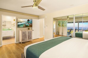 A hotel room with a bed, a television, a ceiling fan, a view of the ocean through a sliding door, and a bathroom with a shower and toilet. - Gorgeous Kaanapali 3BR with Dreamy Ocean Views (Lahaina)