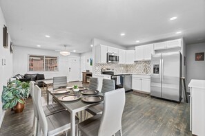 A modern kitchen with white cabinetry, a stainless steel refrigerator, and a microwave. - Downtown Retreat for 12 with Air Hockey (Colorado Springs)