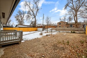 A residential backyard with a wooden deck, a fenced area, and a house in the background. - Downtown Retreat for 12 with Air Hockey (Colorado Springs)