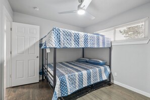 A bunk bed with a patterned bedspread, a ceiling fan, and a window with blinds. - Downtown Retreat for 12 with Air Hockey (Colorado Springs)