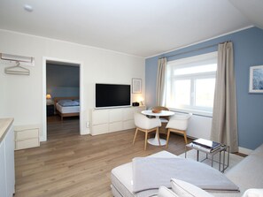 Ein modernes Hotelzimmer mit einem Flachbildfernseher, einem Essbereich mit Stühlen, einem Sofa und einem Fenster mit Vorhängen.