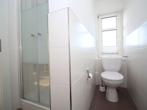 Ein Badezimmer mit Duschkabine aus Glas, Toilette und Fenster.