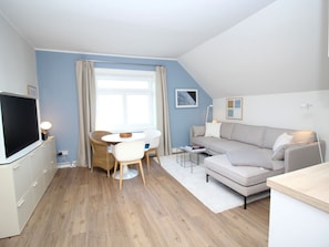 Ein modernes Wohnzimmer mit Fernseher, einem runden Esstisch mit Stühlen, einer Couch und einem Couchtisch.