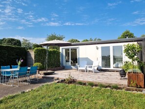 Eine moderne Außenpatio mit Tisch, Stühlen, einem großen Sonnenschirm und einer gläsernen Struktur.