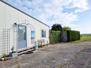 Ein eingeschossiges Gebäude mit einer Veranda, einer Bank und einem Tor zu einer Hecke.