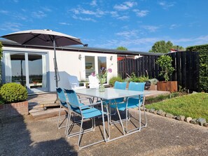 Eine Terrasse mit Tisch und Stühlen, einem überdachten Sonnenschirm und einem Holzzaun.