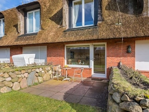 A two-story house with a thatched roof, a stone wall, and a patio with outdoor furniture. - Small Sea Suite (Kampen)