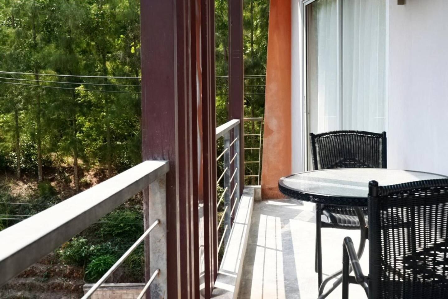 Un balcón con una mesa y sillas, barandilla y vista a árboles.
