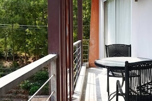Un balcón con una mesa y sillas, barandilla y vista a árboles.