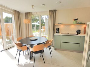 A modern kitchen with a dining area, featuring a round table with chairs, a coffee machine, and a view of the outdoors. - Holiday Home Zone (Callantsoog)