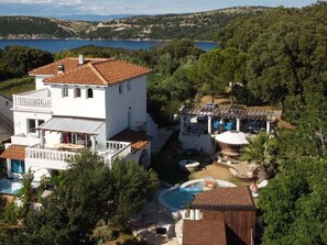 A white villa with a swimming pool, surrounded by greenery and a view of a lake. - Villa Agata With Private Pool and Sauna (Rab)