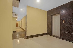 Um corredor com piso de mármore, uma porta com painel de controle e uma parede com padrão texturizado.