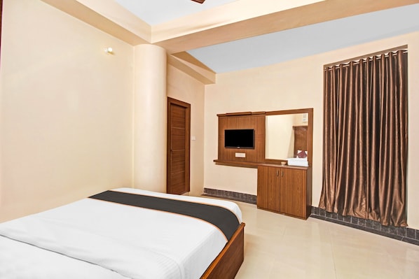 Quarto de hotel com cama, televisão na parede, guarda-roupa de madeira e cortina.
